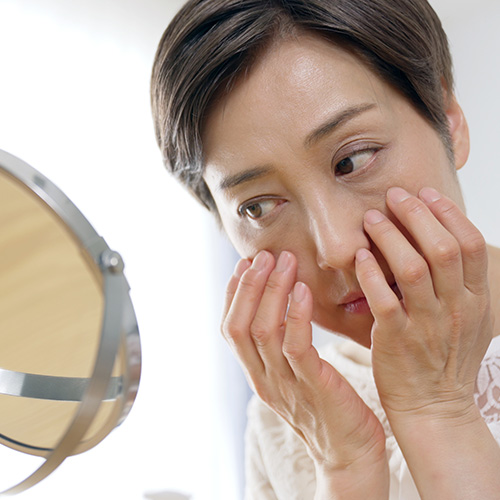 Middle-aged woman examining enlarged pores and sagging skin in mirror, solutions for aging skin care